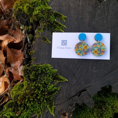 Brincos redondos coloridos em cartão branco sobre tronco com musgo