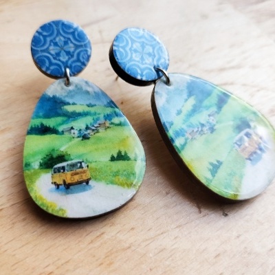 Par de brincos com base azul e pendente em forma de gota com imagem de paisagem e carrinha amarela.