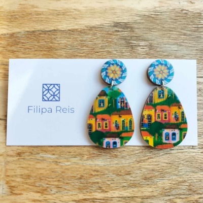 brincos pendentes com design colorido de casas e flor, cartão Filipa Reis sobre madeira