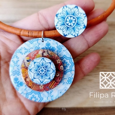 Colar com pendente redondo colorido segurado numa mão com texto de marca ao lado