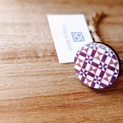 Anel com padrão geométrico em tons roxos e etiqueta com texto Filipa Reis