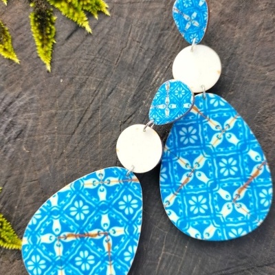 Brincos com padrão azul e branco em forma de gota sobre fundo escuro