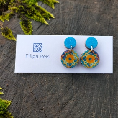 Brincos azuis e florais em cartão branco com texto 'Filipa Reis' sobre madeira rústica