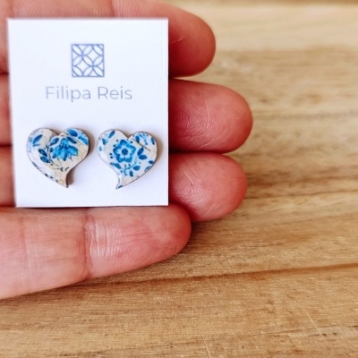 Brincos em forma de coração com padrão floral azul e creme num cartão branco com texto
