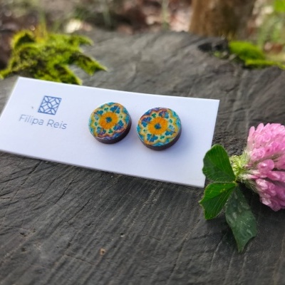 Brincos redondos com padrão floral em embalagem branca perto de flor rosa