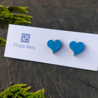 Brincos em forma de coração azul em cartão branco com logótipo 'Filipa Reis' sobre madeira com musgo