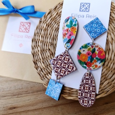 Brincos com padrões florais e geométricos em cartão branco, sobre suporte de palha circular