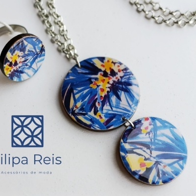 Conjunto de anel e colar com pingentes florais azuis em madeira e cordão metálico.