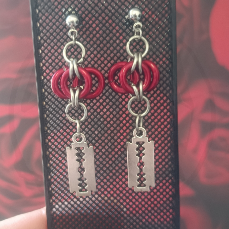Brincos pendentes com argolas vermelhas e lâminas prateadas em suporte preto