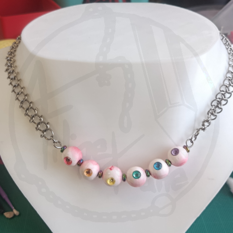 Colar com corrente prateada e contas brancas coloridas num busto branco