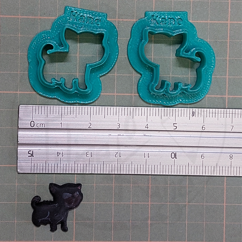 Dois cortadores de biscoitos azuis com formato de cão e uma pequena figura preta de cão com régua e superfície quadriculada