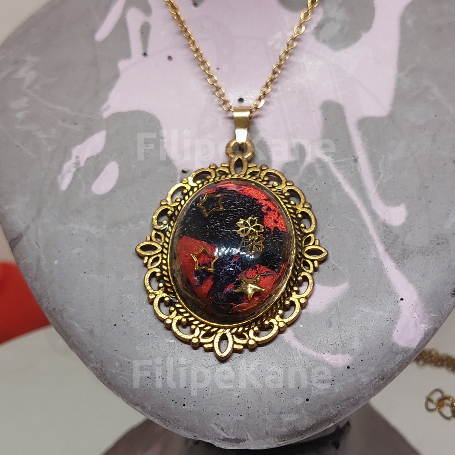 Colar com pendente oval dourado com interior preto e vermelho decorado com estrelas douradas