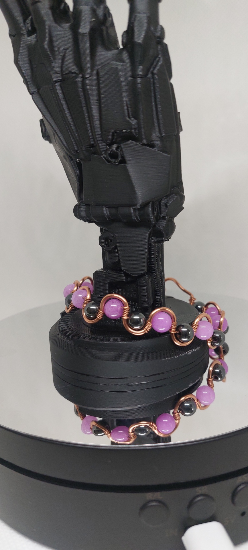 Pulseira com esferas roxas e pretas em arame dourado num suporte preto