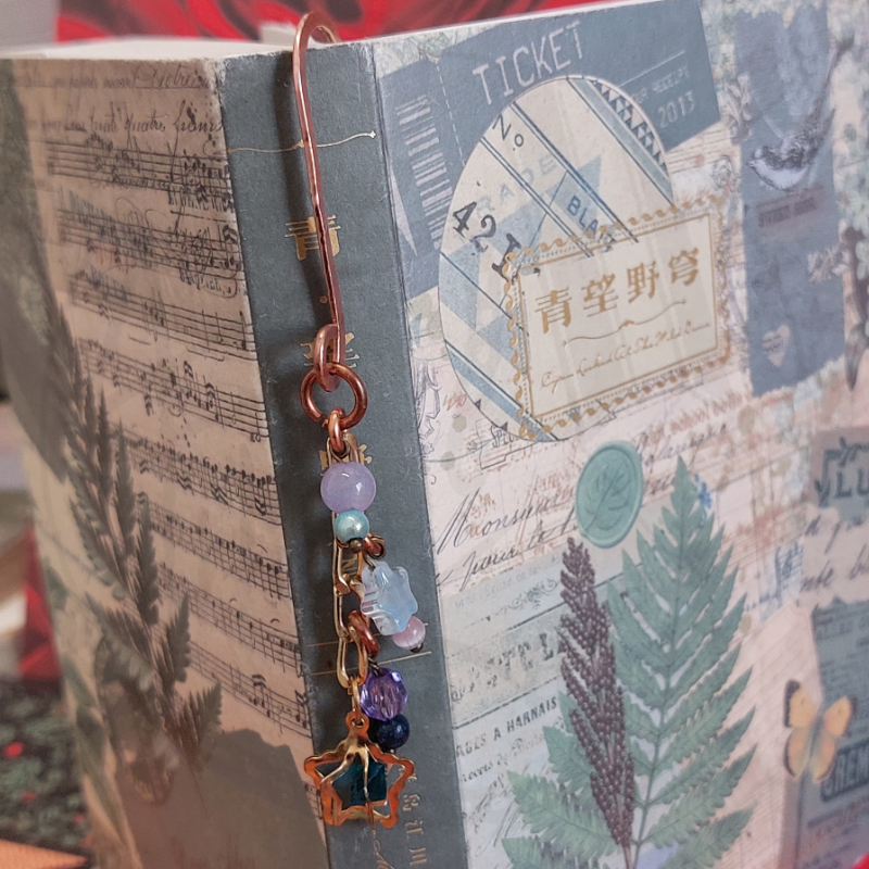 Marcador de livros metálico com pedras coloridas pendurado numa capa de livro decorada