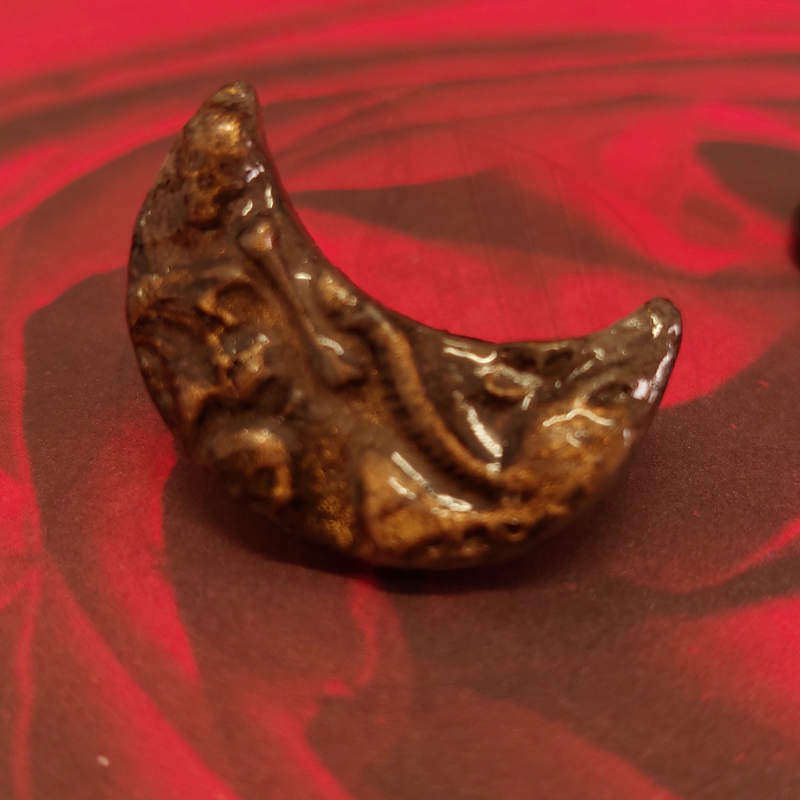 Peça cerâmica castanha em forma de meia-lua com relevo sobre fundo vermelho e negro