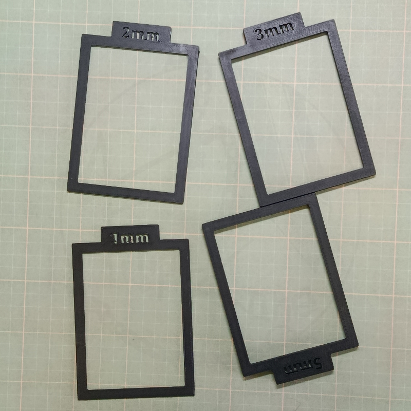 Molduras retangulares pretas com etiquetas 1mm, 2mm, 3mm e 5mm sobre superfície quadriculada verde