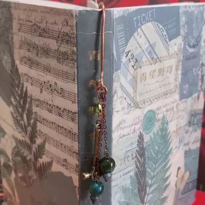 Marcador de livro em metal com contas verdes e capa de livro decorada com partituras e plantas