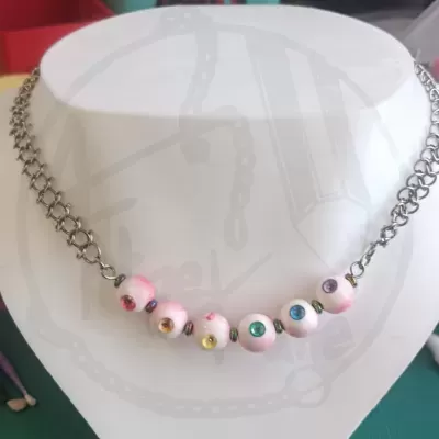 Colar com corrente prateada e contas brancas coloridas num busto branco