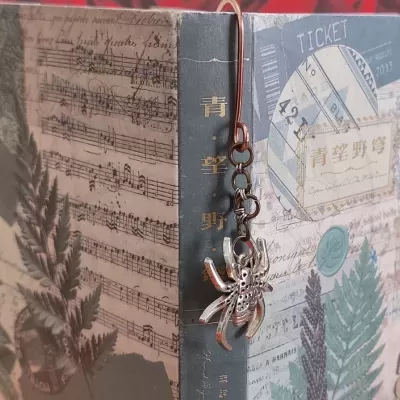 Marcador de livros com pendente de aranha sobre livro decorado com folhas e partituras