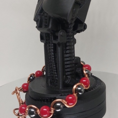 Pulseira com bolas vermelhas e cinzentas em fio de cobre numa mão robótica negra.