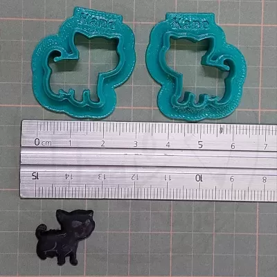 Dois cortadores de biscoitos azuis com formato de cão e uma pequena figura preta de cão com régua e superfície quadriculada