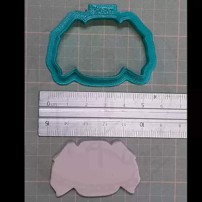 Cortador de bolachas verde, régua metálica e massa moldada no fundo quadriculado