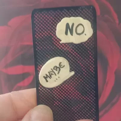 Estojo preto com padrão de grelha diagonal decorado com dois balões de fala com texto NO. e MAYBE
