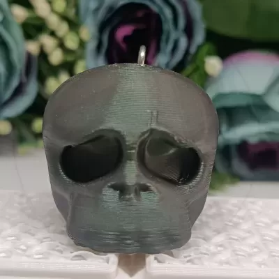 Pendente caveira preto em plástico com textura sobre base branca com flores ao fundo