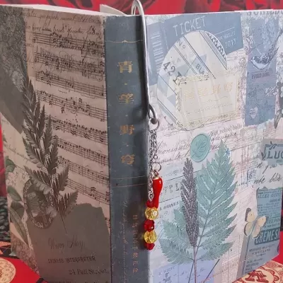 Livro decorativo com folhas de samambaia, partituras e marcador com contas coloridas