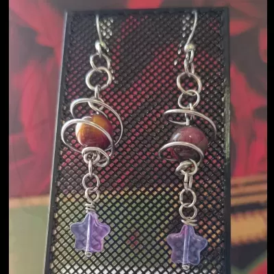 Brincos com hastes prateadas, esfera colorida e pendente estrela lilás.
