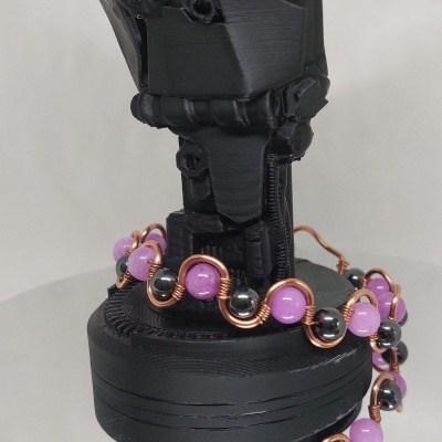 Pulseira com esferas roxas e pretas em arame dourado num suporte preto