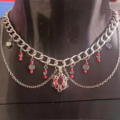 Colar prata com pendentes vermelhos e prateados numa exposição.