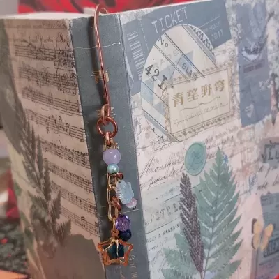 Marcador de livros metálico com pedras coloridas pendurado numa capa de livro decorada