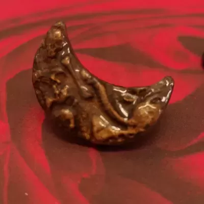 Peça cerâmica castanha em forma de meia-lua com relevo sobre fundo vermelho e negro