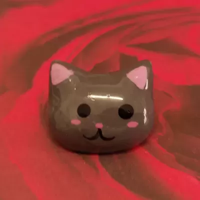Figura decorativa cinzenta em forma de cabeça de gato com detalhes cor-de-rosa sobre fundo vermelho.