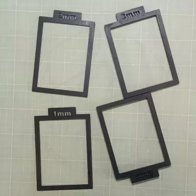 Molduras retangulares pretas com etiquetas 1mm, 2mm, 3mm e 5mm sobre superfície quadriculada verde