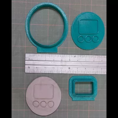 Peças para impressão 3D em plástico azul e cinzento com régua e fundo quadriculado.