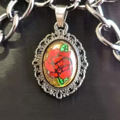 Colar com corrente prateada e pendente oval com desenho de rosa vermelha e fundo dourado