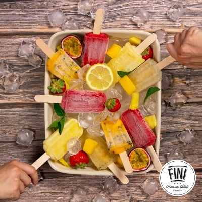 Gelados coloridos em pau numa bacia com gelo sobre mesa de madeira rústica