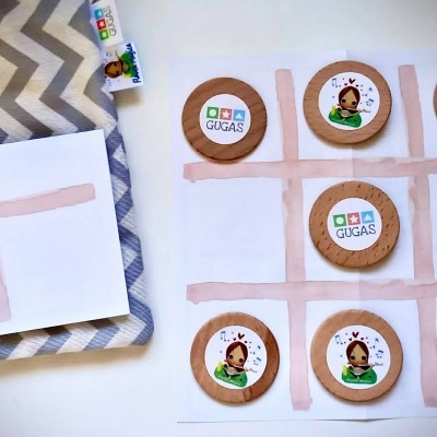 Jogo da velha com peças de cartão decoradas e bandeja cinza com padrão zig-zag