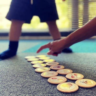 Peças redondas de madeira com imagens de alimentos sobre tapete cinzento com mão a apontar