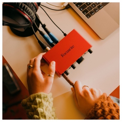 Interface de áudio Focusrite vermelha com cabos ligada ao lado de portátil