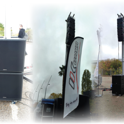 Colunas de som profissionais pretas empilhadas e em estruturas metálicas ao ar livre com bandeira branca com texto 'conraco'.