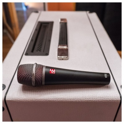 Microfone preto com visor vermelho digital sobre amplificador cinza