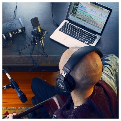 homem com auscultadores a tocar guitarra frente a computador e microfones