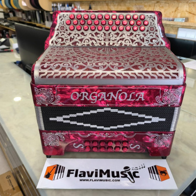 Acordeão vermelho decorativo com botões e ornamentos prateados, marca ORGANOLA visível, colocado numa loja musical.