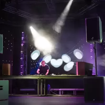 DJ num palco com colunas de som grandes e luzes coloridas