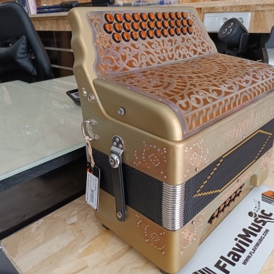 Acordeão dourado com botões pretos em mesa de madeira com cartaz FlaviMusic