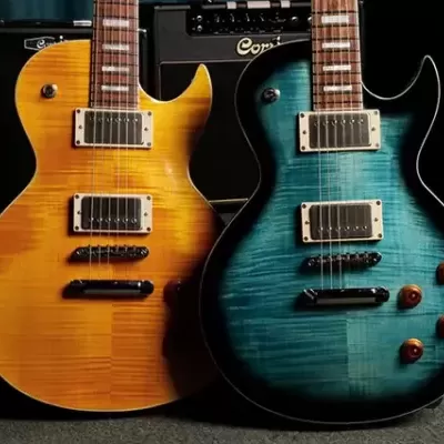 Duas guitarras elétricas flamejadas, amarelo âmbar e azul esverdeado, com captadores humbucker e botões marrons, apoiadas num tapete cinza