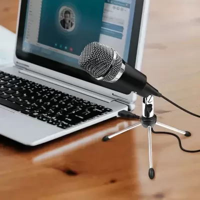 Microfone preto com suporte metálico em frente a computador portátil